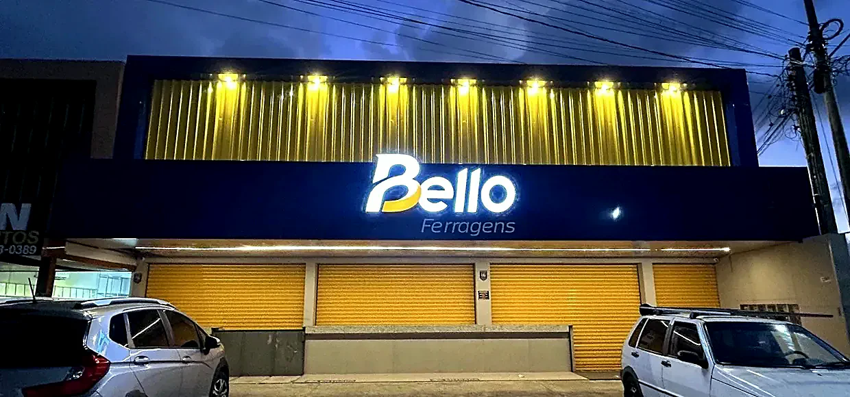 Fotografia real da mesma fachada depois, com ACM azul, letra caixa iluminada e faixa dourada acesa à noite