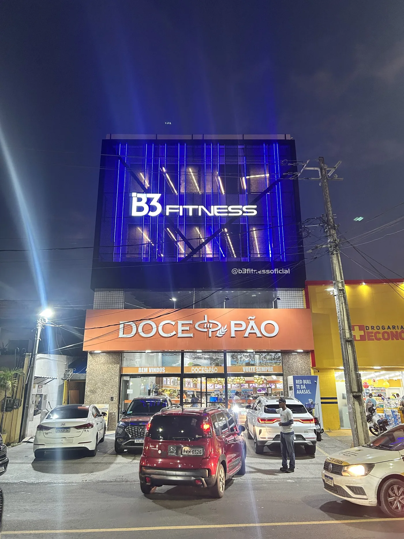 Prédio da B3 Fitness aceso à noite, brises em LED azul e letra caixa iluminada