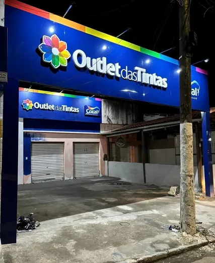 Fachada azul iluminada do Outlet das Tintas com faixa de espectro de cores