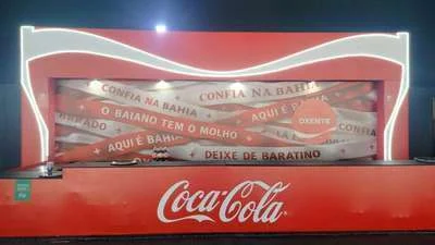 Estrutura com fitas de frases baianas iluminadas sobre balcão, ativação da Coca-Cola