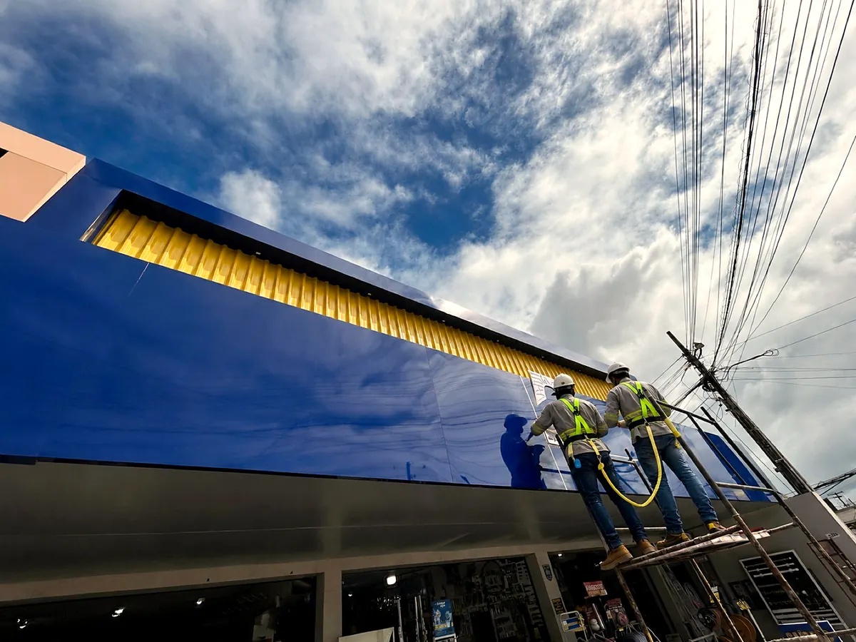 Equipe própria da COMUNIKAR instalando revestimento em ACM com andaime, capacete e cinto paraquedista