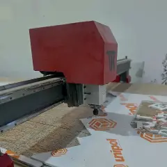 Fresa CNC recortando chapa rígida sobre a bancada, com o material impresso já posicionado